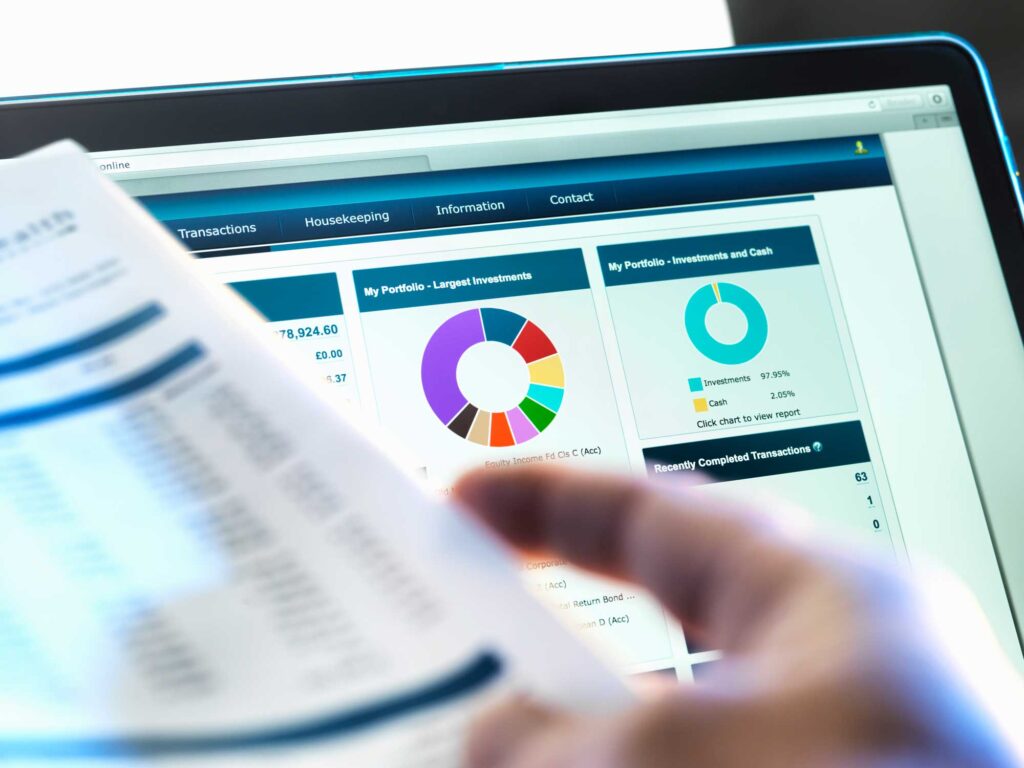 financial-reporting investor is reviewing numbers on a document with financial graphs on a computer in the background