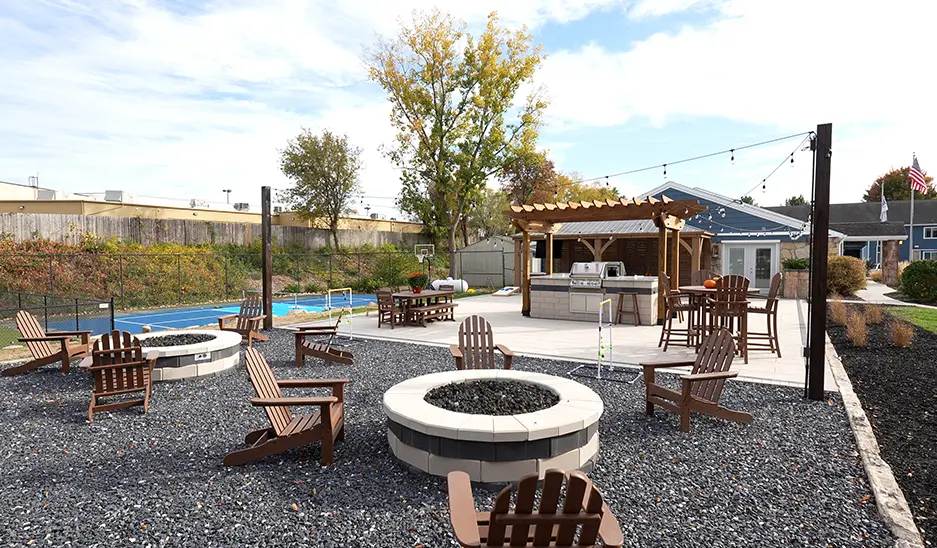 firepits with lounge chairs in the foreground, with an outdoor barbecue and pickleball court are in the background